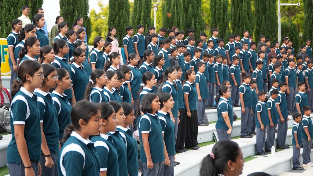 Students in school uniform gathered on outdoor bleachers during a school assembly at TACS